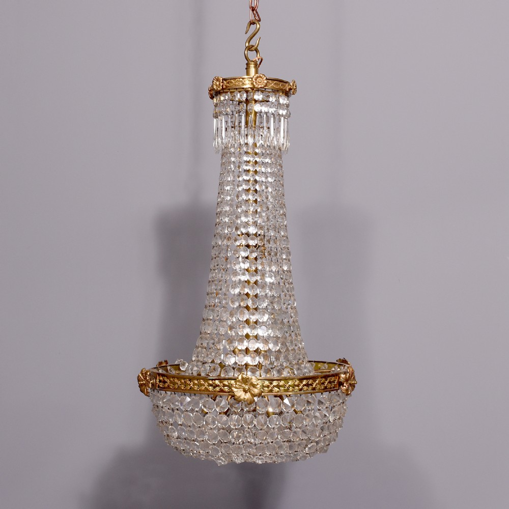 An Empire style brass and glass chandelier featuring a cascading tent of clear glass beads, decorative brass leaf mounts, and a lower rounded glass basket.