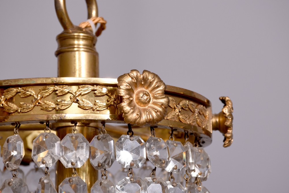 An Empire style brass and glass chandelier featuring a cascading tent of clear glass beads, decorative brass leaf mounts, and a lower rounded glass basket. View II
