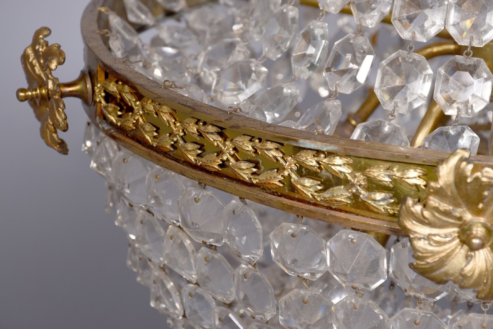 An Empire style brass and glass chandelier featuring a cascading tent of clear glass beads, decorative brass leaf mounts, and a lower rounded glass basket. View IV
