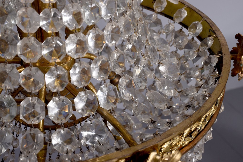 An Empire style brass and glass chandelier featuring a cascading tent of clear glass beads, decorative brass leaf mounts, and a lower rounded glass basket. View V