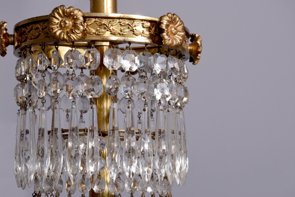 An Empire style brass and glass chandelier featuring a cascading tent of clear glass beads, decorative brass leaf mounts, and a lower rounded glass basket. View VI