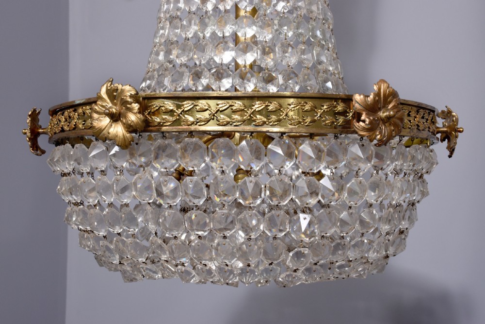 An Empire style brass and glass chandelier featuring a cascading tent of clear glass beads, decorative brass leaf mounts, and a lower rounded glass basket. View VII