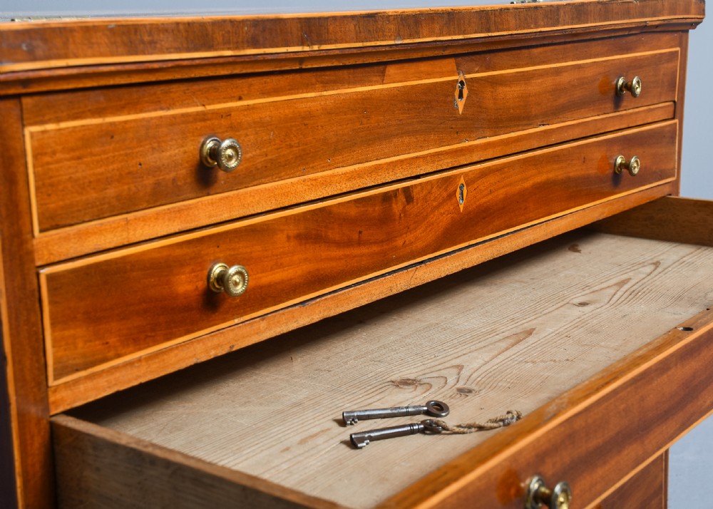An 18th-century George III mahogany floor-standing folio cabinet featuring shallow drawers with brass knobs, boxwood inlay, brass side carrying handles, and shaped bracket feet. View III