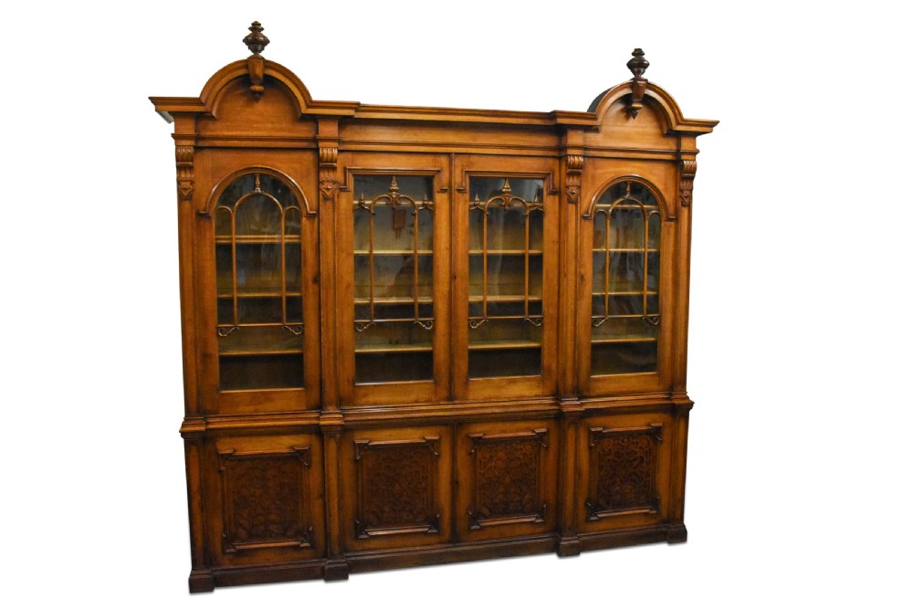 A large Mid-Victorian carved wooden glazed bookcase featuring four upper cabinet doors with arch tracery and four lower panelled cupboard doors topped with decorative finials. View III