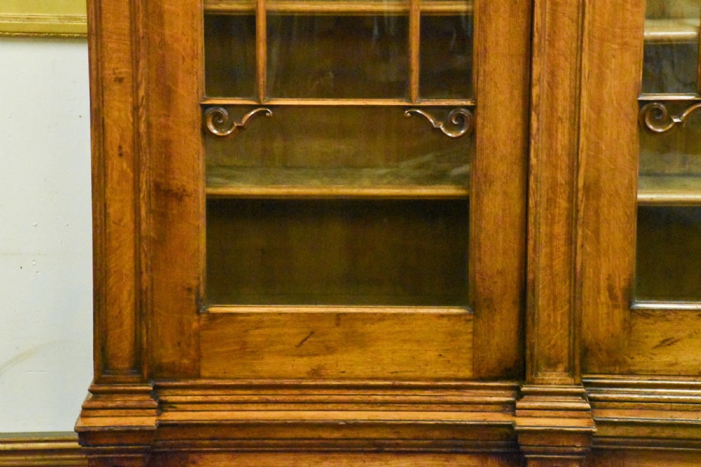 A large Mid-Victorian carved wooden glazed bookcase featuring four upper cabinet doors with arch tracery and four lower panelled cupboard doors topped with decorative finials. View V