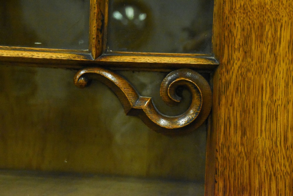 A large Mid-Victorian carved wooden glazed bookcase featuring four upper cabinet doors with arch tracery and four lower panelled cupboard doors topped with decorative finials. View VII