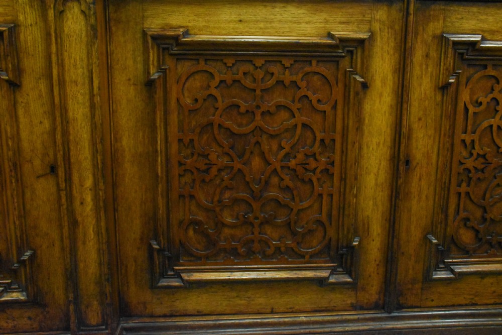 A large Mid-Victorian carved wooden glazed bookcase featuring four upper cabinet doors with arch tracery and four lower panelled cupboard doors topped with decorative finials. View X