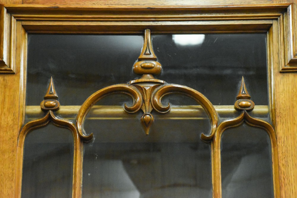 A large Mid-Victorian carved wooden glazed bookcase featuring four upper cabinet doors with arch tracery and four lower panelled cupboard doors topped with decorative finials. View XII