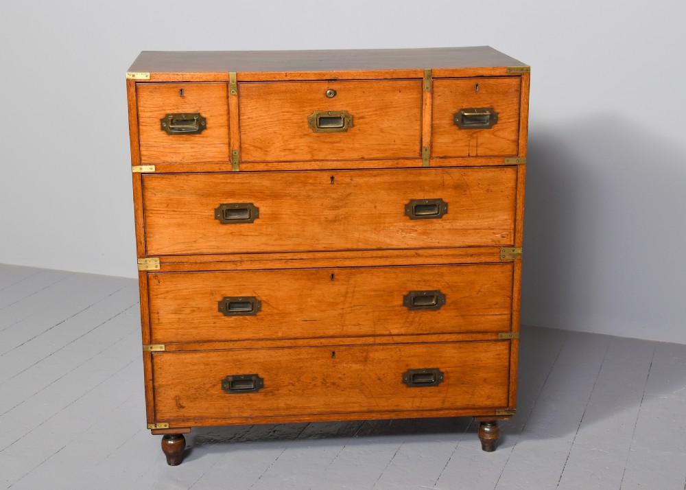 A nineteenth-century two-part teak military campaign chest of drawers featuring flush brass handles, protective brass corner brackets, and turned feet.
