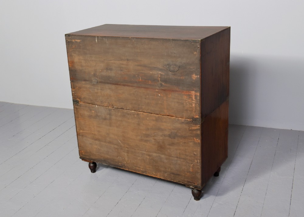 A nineteenth-century two-part teak military campaign chest of drawers featuring flush brass handles, protective brass corner brackets, and turned feet. View X