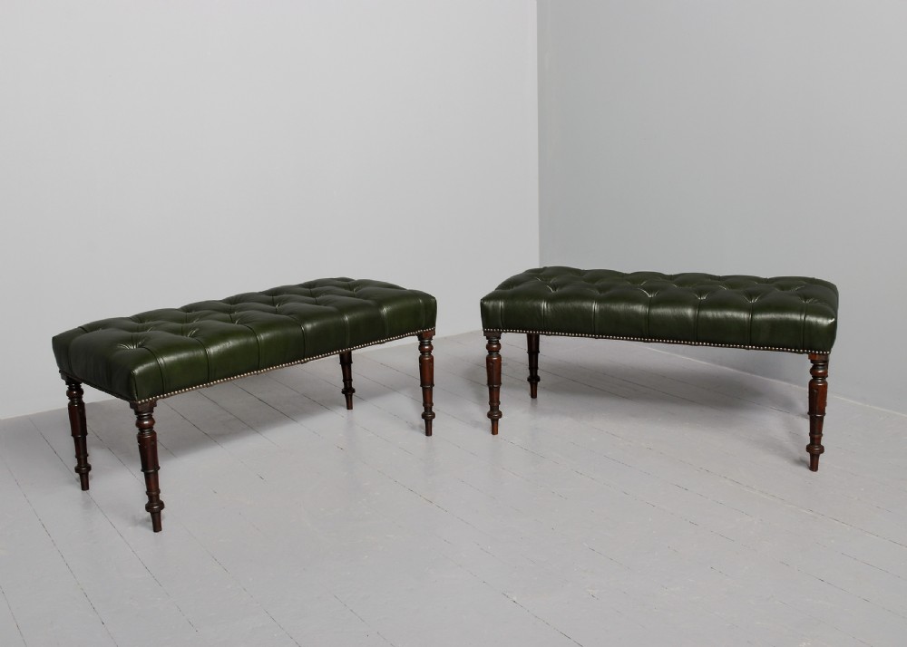 A pair of Regency mahogany benches featuring dark green buttoned leather upholstery trimmed with brass studs, supported by fluted turned legs.