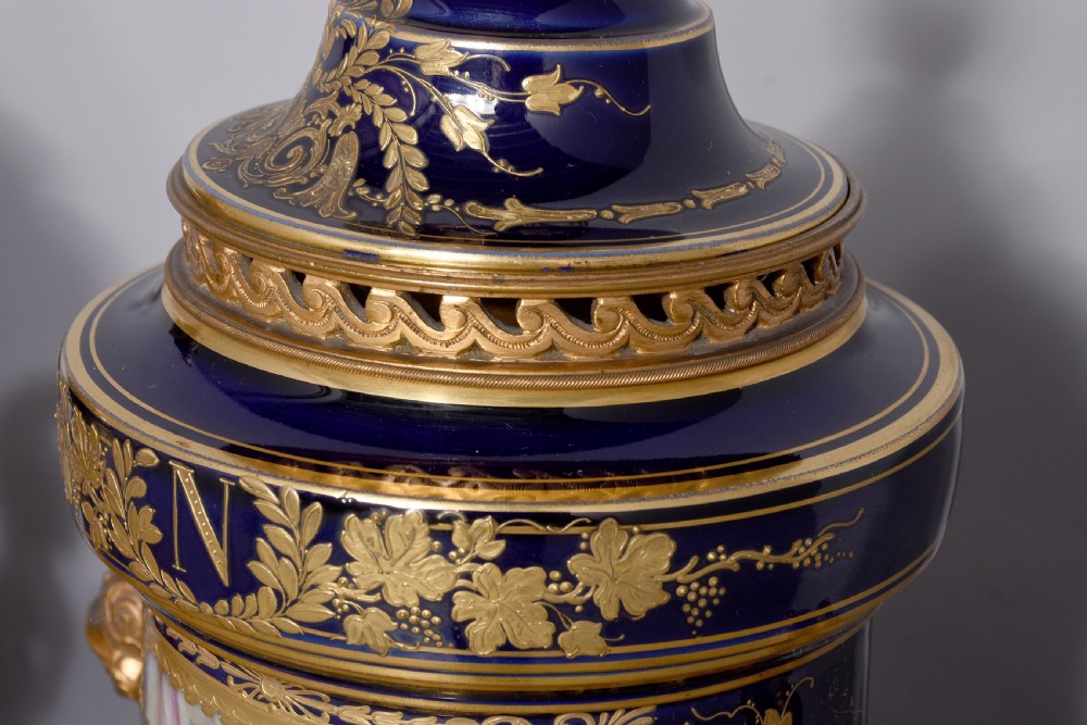 A pair of French cobalt blue porcelain lidded urns with intricate gilding, hand-painted Napoleonic historical scenes, and gilt bronze helmeted bust handles topped with eagle finials. View II