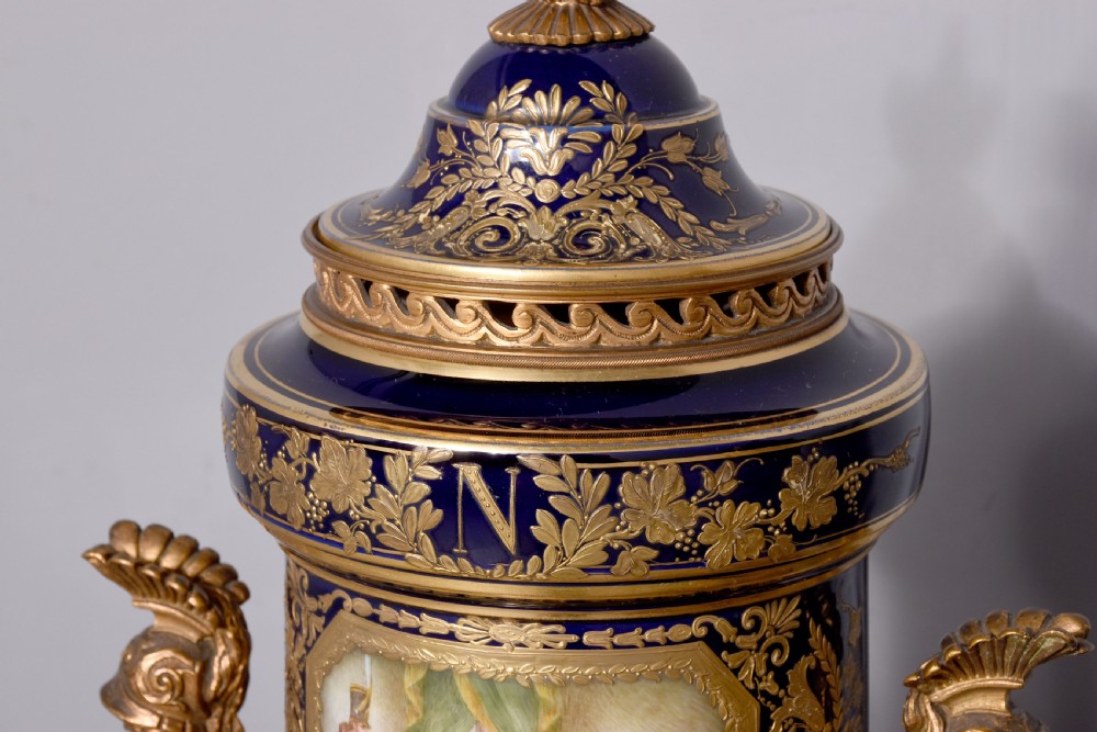 A pair of French cobalt blue porcelain lidded urns with intricate gilding, hand-painted Napoleonic historical scenes, and gilt bronze helmeted bust handles topped with eagle finials. View III