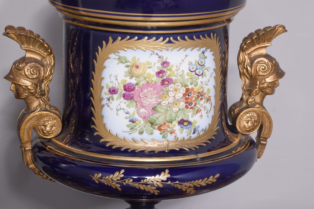 A pair of French cobalt blue porcelain lidded urns with intricate gilding, hand-painted Napoleonic historical scenes, and gilt bronze helmeted bust handles topped with eagle finials. View VI