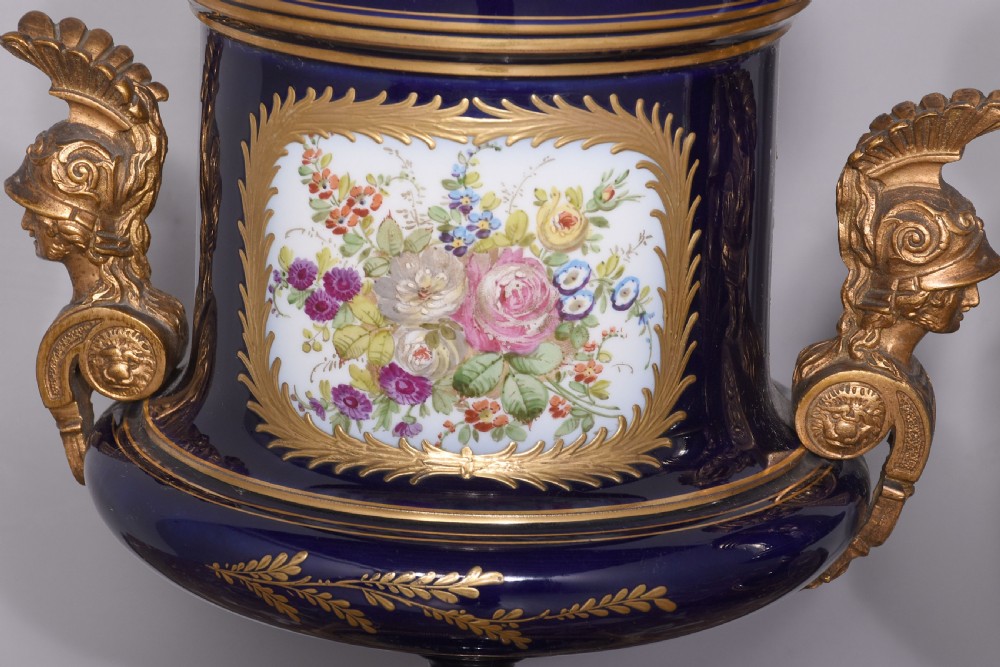 A pair of French cobalt blue porcelain lidded urns with intricate gilding, hand-painted Napoleonic historical scenes, and gilt bronze helmeted bust handles topped with eagle finials. View VII