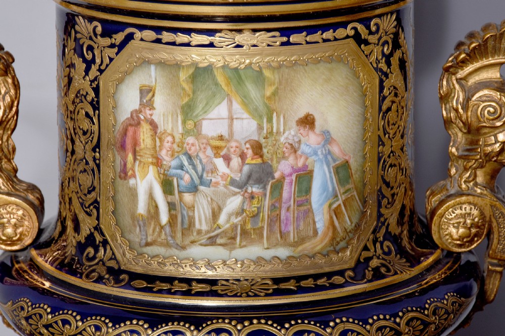 A pair of French cobalt blue porcelain lidded urns with intricate gilding, hand-painted Napoleonic historical scenes, and gilt bronze helmeted bust handles topped with eagle finials. View VIII