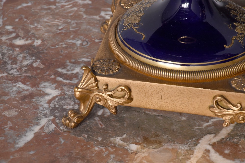 A pair of French cobalt blue porcelain lidded urns with intricate gilding, hand-painted Napoleonic historical scenes, and gilt bronze helmeted bust handles topped with eagle finials. View X