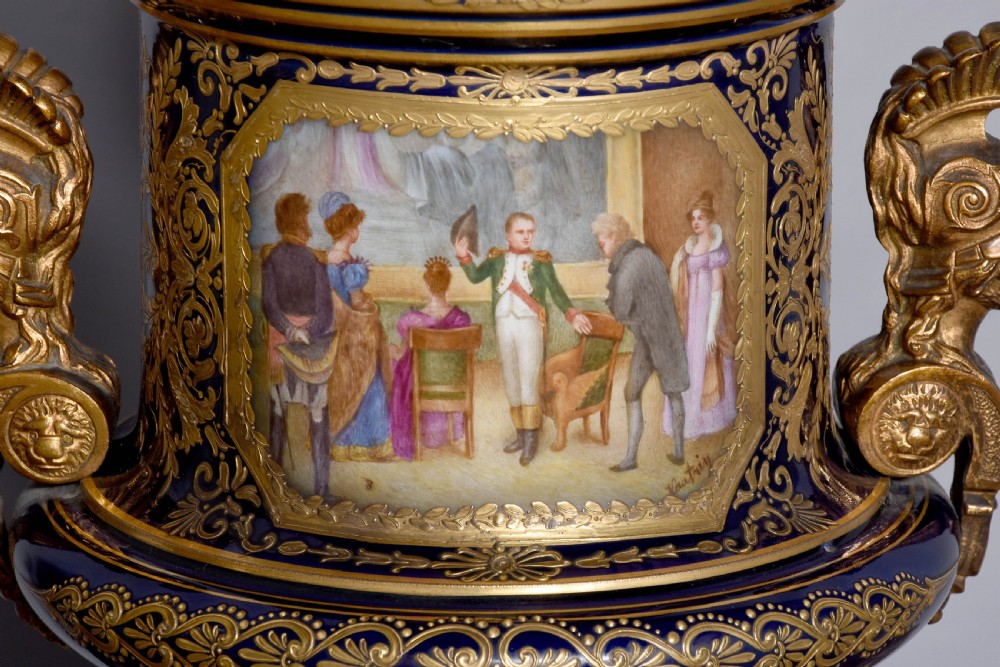 A pair of French cobalt blue porcelain lidded urns with intricate gilding, hand-painted Napoleonic historical scenes, and gilt bronze helmeted bust handles topped with eagle finials. View XIII