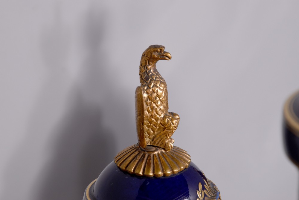 A pair of French cobalt blue porcelain lidded urns with intricate gilding, hand-painted Napoleonic historical scenes, and gilt bronze helmeted bust handles topped with eagle finials. View XVI