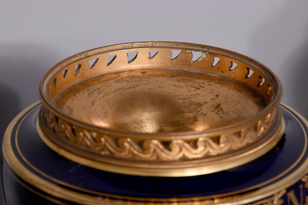 A pair of French cobalt blue porcelain lidded urns with intricate gilding, hand-painted Napoleonic historical scenes, and gilt bronze helmeted bust handles topped with eagle finials. View XVIII