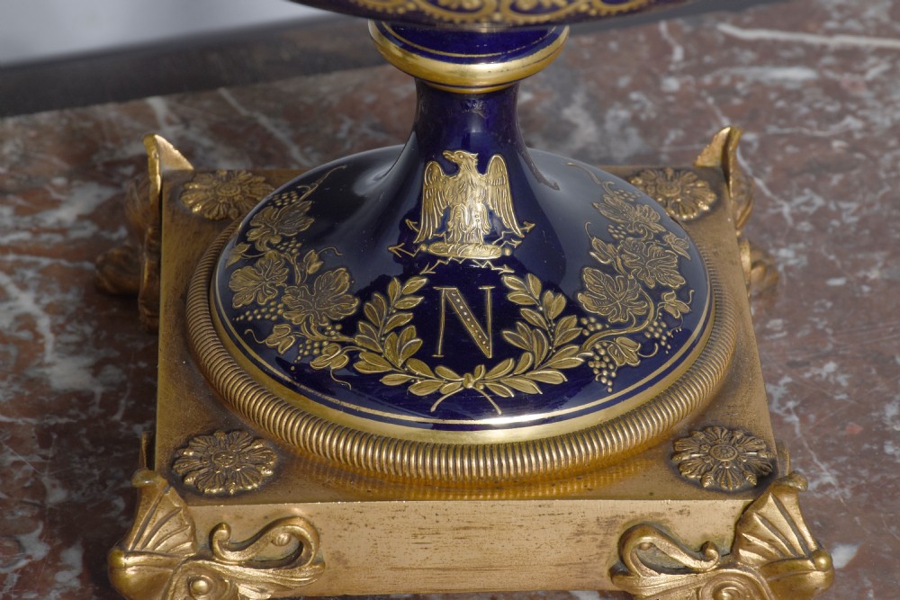 A pair of French cobalt blue porcelain lidded urns with intricate gilding, hand-painted Napoleonic historical scenes, and gilt bronze helmeted bust handles topped with eagle finials. View XXII