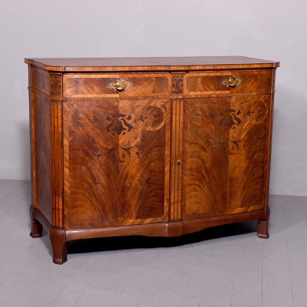 A two-door wooden folio cabinet with dark marquetry scroll inlay, upper drawers with ornate brass handles, and short shaped legs.