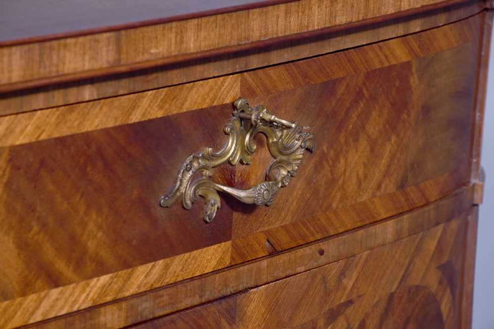 A two-door wooden folio cabinet with dark marquetry scroll inlay, upper drawers with ornate brass handles, and short shaped legs. View V