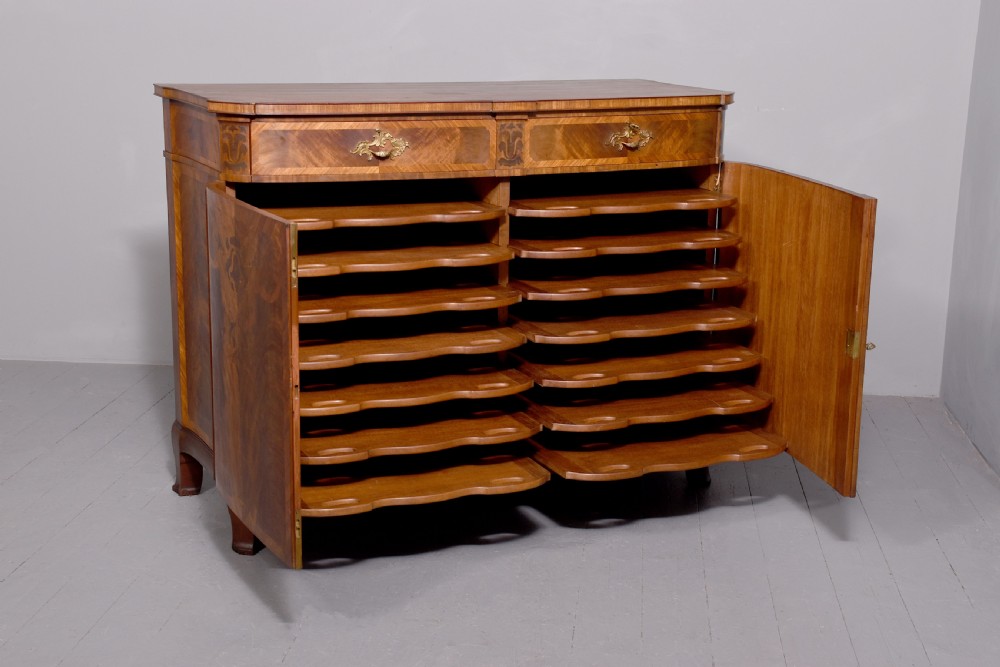 A two-door wooden folio cabinet with dark marquetry scroll inlay, upper drawers with ornate brass handles, and short shaped legs. View IX