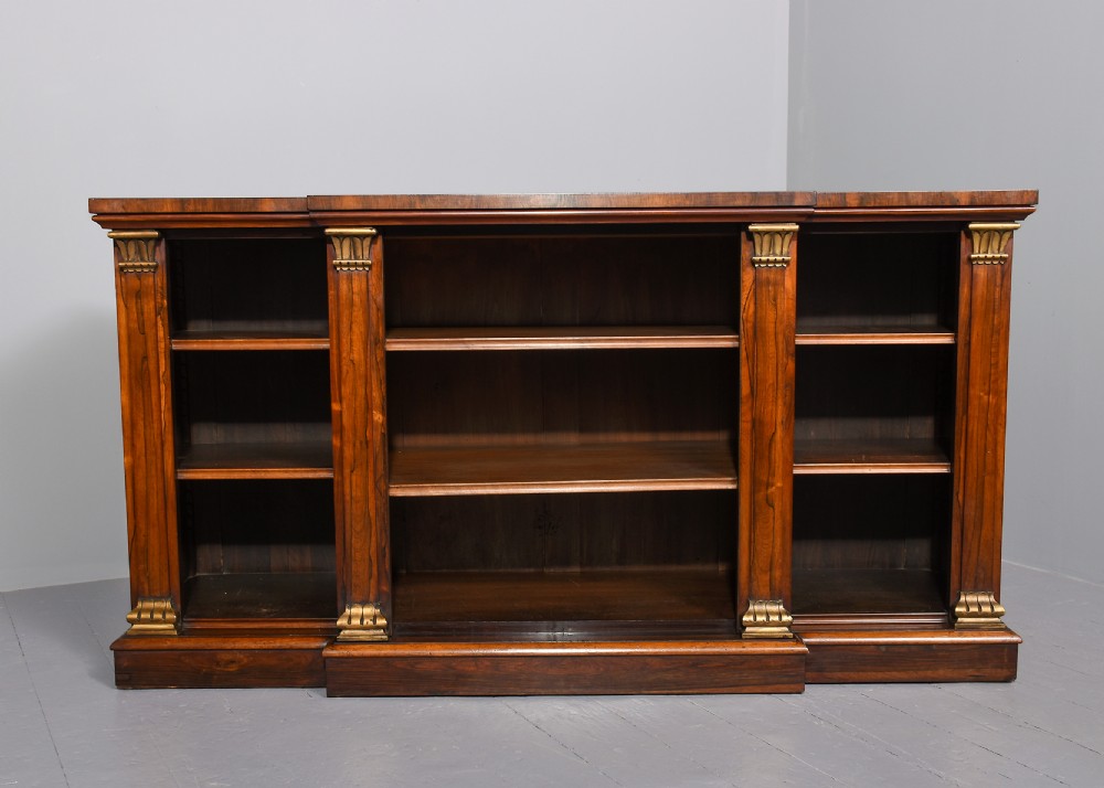 An antique open breakfront bookcase constructed from dark rosewood with gilded carved capitals and filled with leather-bound books. View II