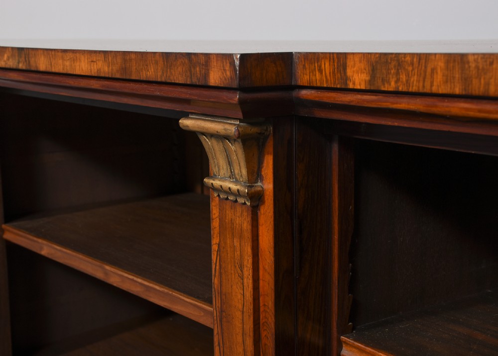 An antique open breakfront bookcase constructed from dark rosewood with gilded carved capitals and filled with leather-bound books. View VI