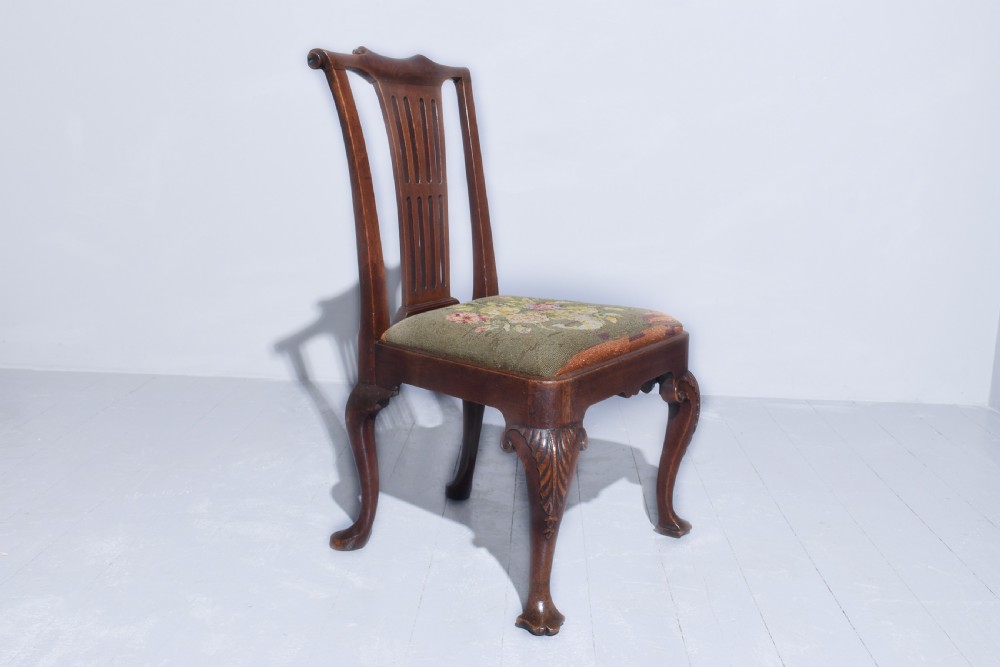 A George II walnut side chair featuring a pierced back splat, floral needlepoint seat, and carved cabriole legs.