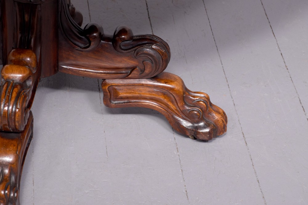 A circular George IV rosewood breakfast table featuring a carved edge, a spiral column pedestal, and a quadruped scrolled base with brass castors. View III