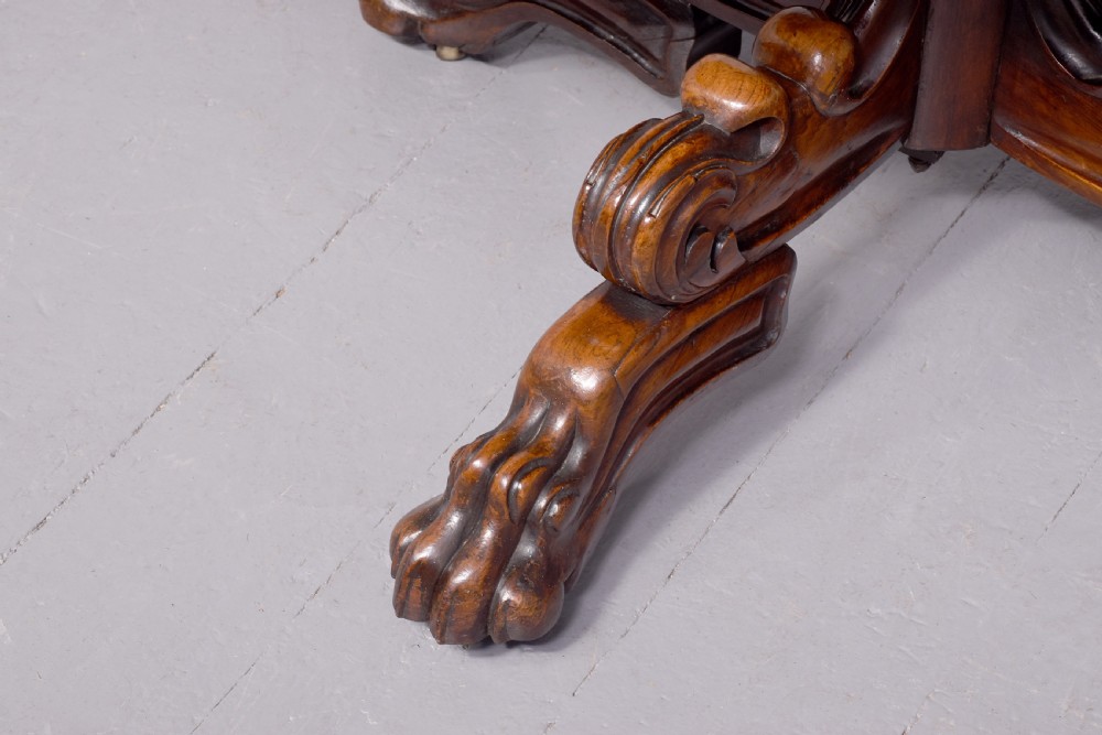 A circular George IV rosewood breakfast table featuring a carved edge, a spiral column pedestal, and a quadruped scrolled base with brass castors. View IV
