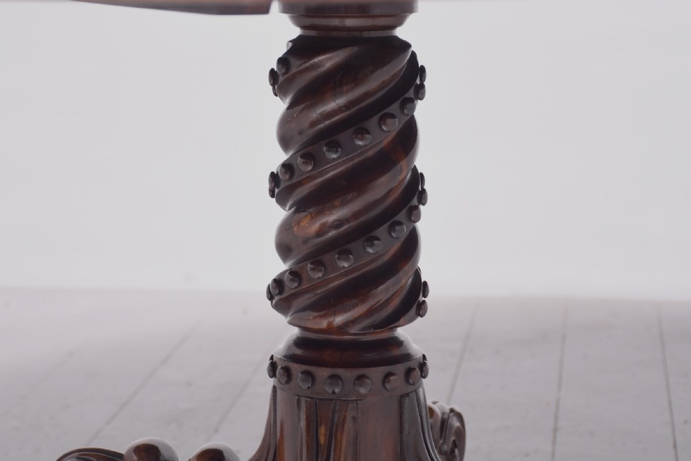 A circular George IV rosewood breakfast table featuring a carved edge, a spiral column pedestal, and a quadruped scrolled base with brass castors. View VI