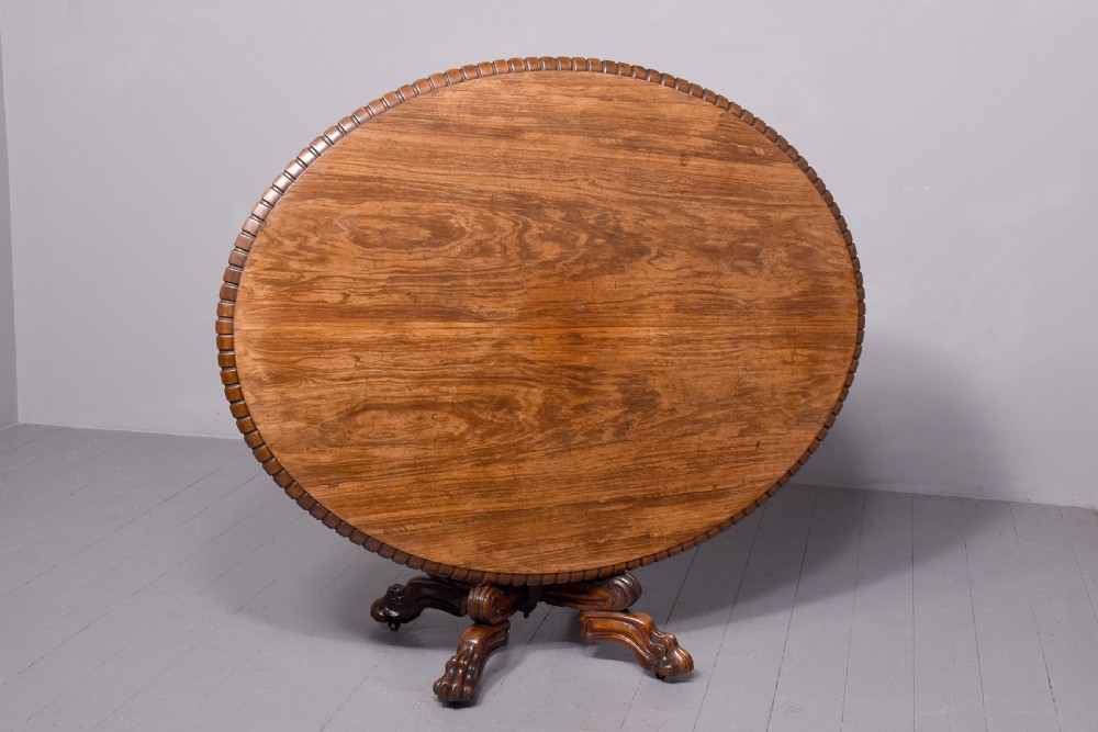 A circular George IV rosewood breakfast table featuring a carved edge, a spiral column pedestal, and a quadruped scrolled base with brass castors. View VII