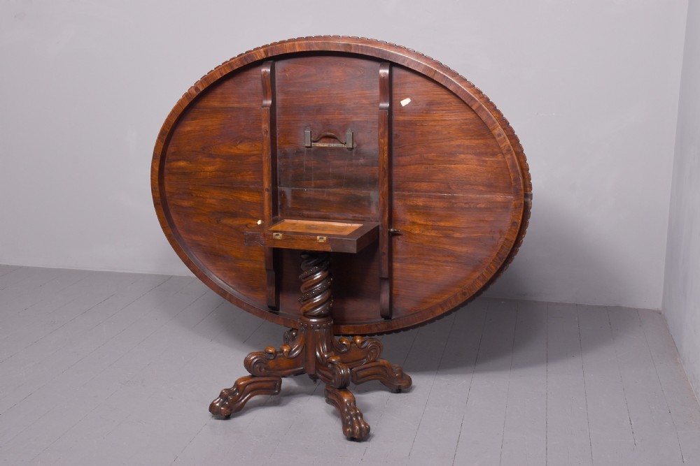 A circular George IV rosewood breakfast table featuring a carved edge, a spiral column pedestal, and a quadruped scrolled base with brass castors. View VIII