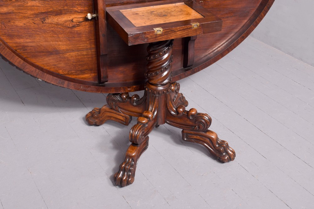 A circular George IV rosewood breakfast table featuring a carved edge, a spiral column pedestal, and a quadruped scrolled base with brass castors. View IX