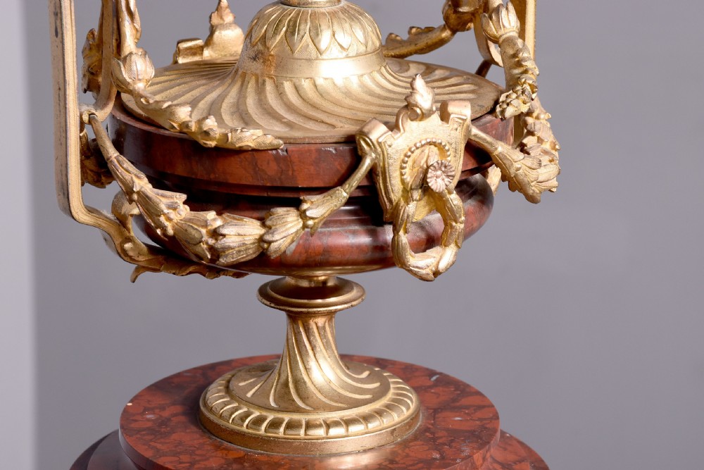 A French Neoclassical style mantel clock featuring a cylindrical rouge marble body with gilt bronze floral swags, a top urn finial, and paw feet. View III