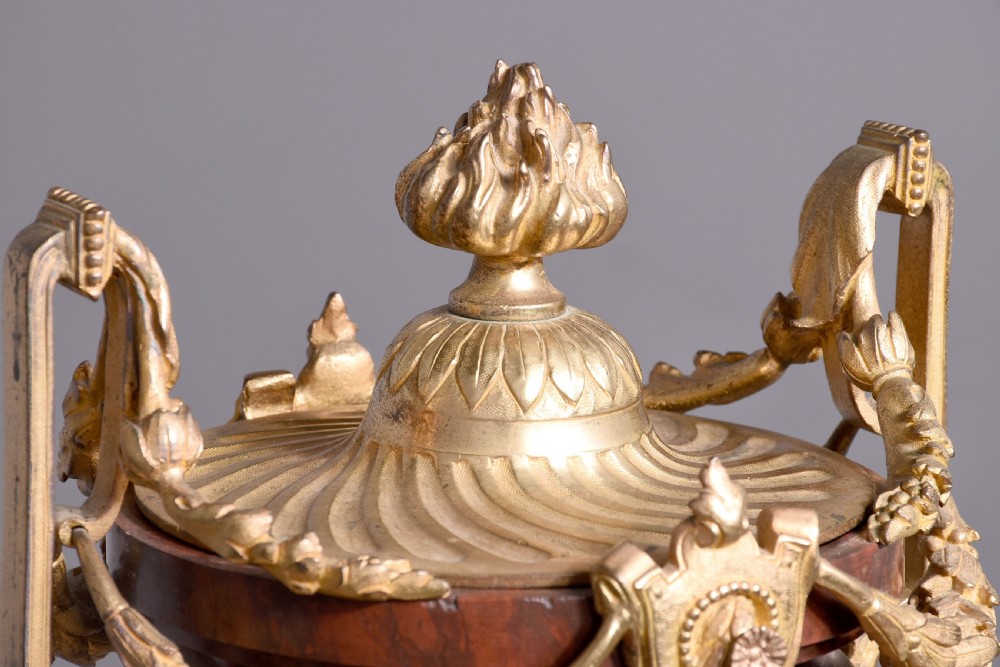 A French Neoclassical style mantel clock featuring a cylindrical rouge marble body with gilt bronze floral swags, a top urn finial, and paw feet. View IV