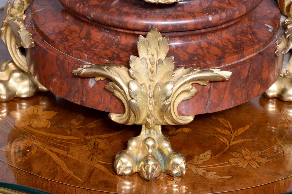 A French Neoclassical style mantel clock featuring a cylindrical rouge marble body with gilt bronze floral swags, a top urn finial, and paw feet. View VII