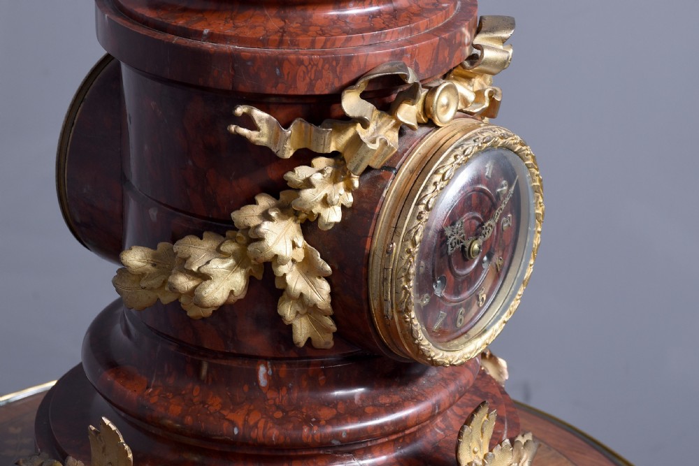 A French Neoclassical style mantel clock featuring a cylindrical rouge marble body with gilt bronze floral swags, a top urn finial, and paw feet. View IX