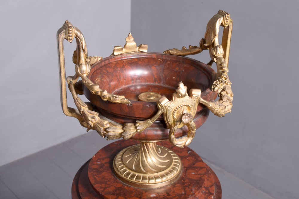 A French Neoclassical style mantel clock featuring a cylindrical rouge marble body with gilt bronze floral swags, a top urn finial, and paw feet. View XII