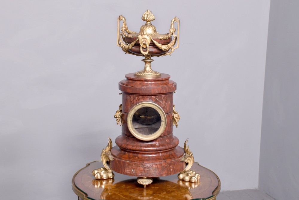 A French Neoclassical style mantel clock featuring a cylindrical rouge marble body with gilt bronze floral swags, a top urn finial, and paw feet. View XIII