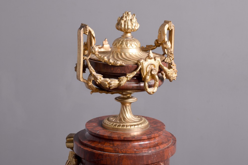A French Neoclassical style mantel clock featuring a cylindrical rouge marble body with gilt bronze floral swags, a top urn finial, and paw feet. View XIV