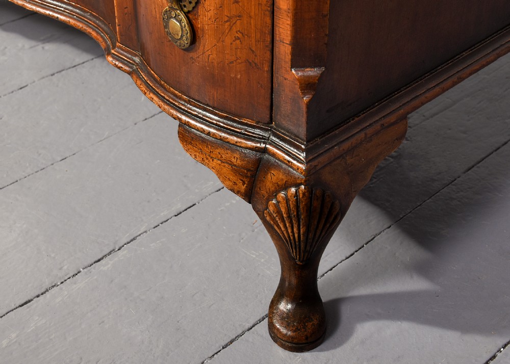 A George II style walnut chest of drawers featuring a contoured front, four drawers with brass handles, and cabriole legs. View V