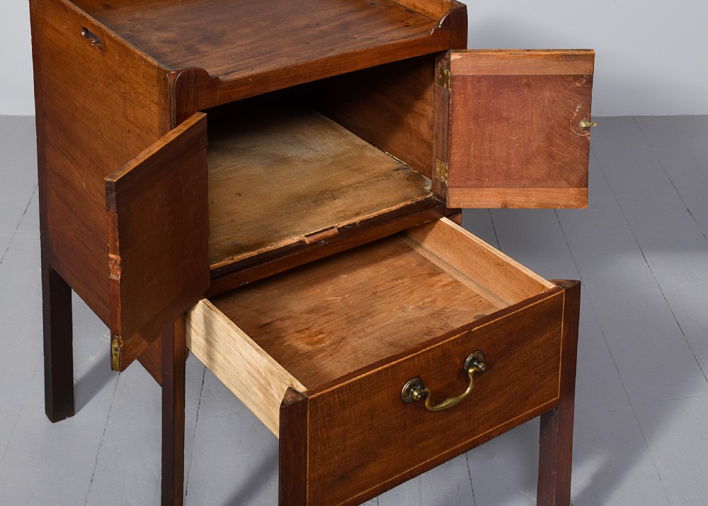 A George III mahogany bedside commode featuring a gallery tray top with cut-out handles, twin flame-mahogany doors, and a single lower drawer on square legs. View IV