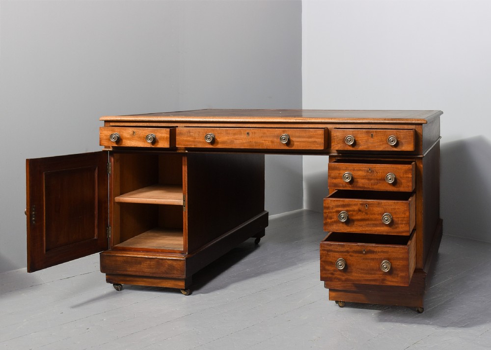 A Georgian style mahogany partners desk featuring a leather writing top, multiple drawers with brass turned knobs, and a pedestal base on castors. View II