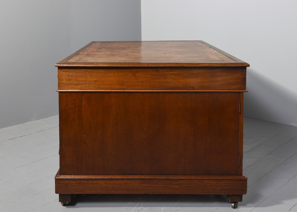 A Georgian style mahogany partners desk featuring a leather writing top, multiple drawers with brass turned knobs, and a pedestal base on castors. View IX