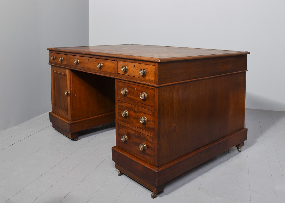 A Georgian style mahogany partners desk featuring a leather writing top, multiple drawers with brass turned knobs, and a pedestal base on castors. View X