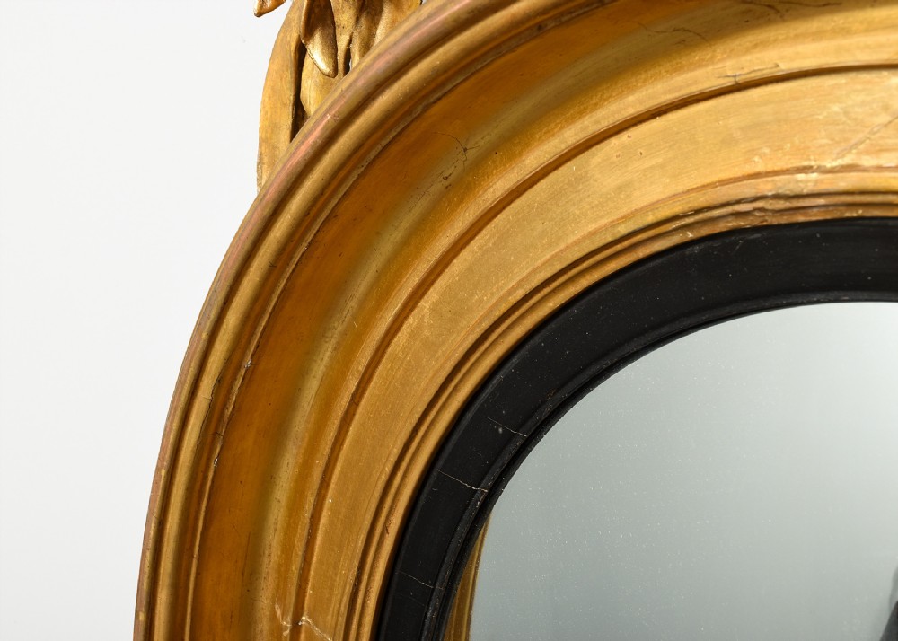 A circular Regency period giltwood convex mirror framed with an ebonised inner slip ring, topped by a carved eagle surmount perched on a pedestal with acanthus leaf accents. View VI